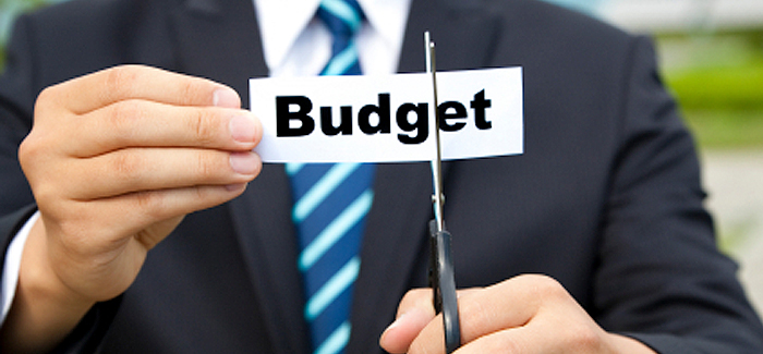Event professional in a suit with scissors cutting a piece of paper with the word budget on it